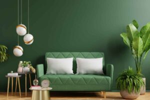 divano verde con cuscini bianchi è posto davanti a un muro verde, di fianco ci sono dei vasi con le piante, lampade sospese e coffee table dorati