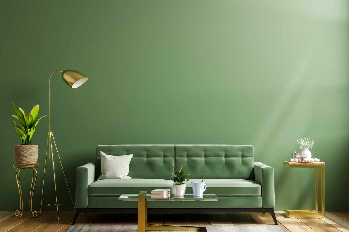 angolo soggiorno in salotto con divano verde, lampade e tavolini in metallo dorato e parete verde