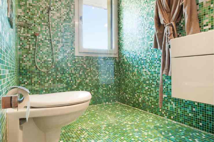 bagno piastrellato interamente a mosaico nelle varie sfumature di verde con mobili sospesi e doccia a filo pavimento