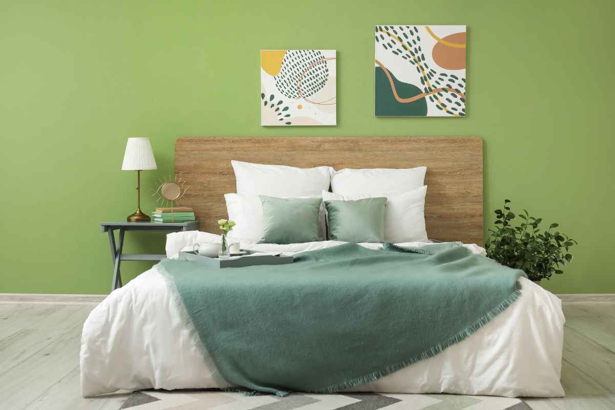 Camera da letto con parete della testata verde, letto con testiera in legno. Il letto ha lenzuola bianche, coperte e cuscini verdi