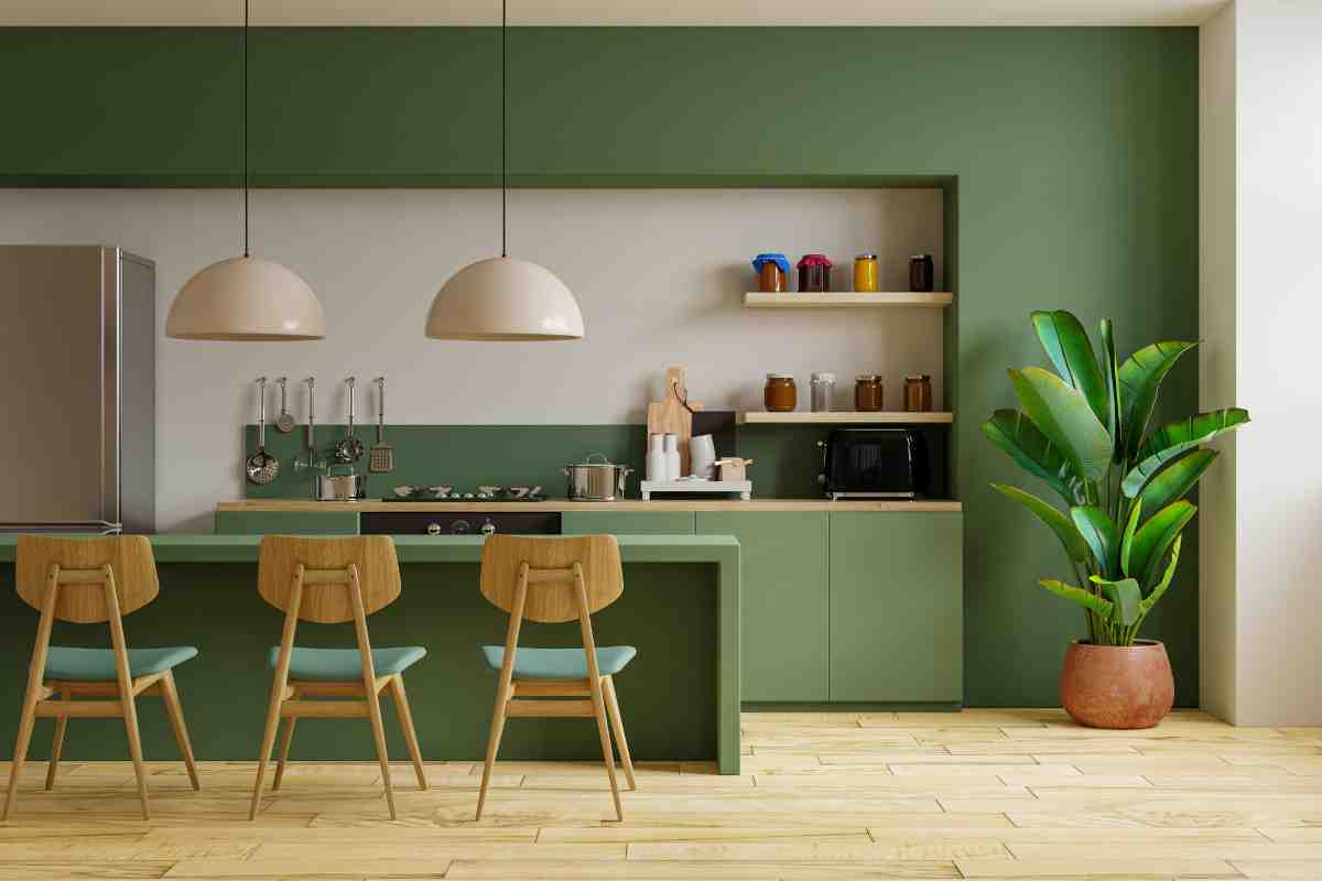 Cucina moderna con isola di colore verde, sedie di legno chiaro con sedili verdi e ampie lampade a sospensione per illuminare