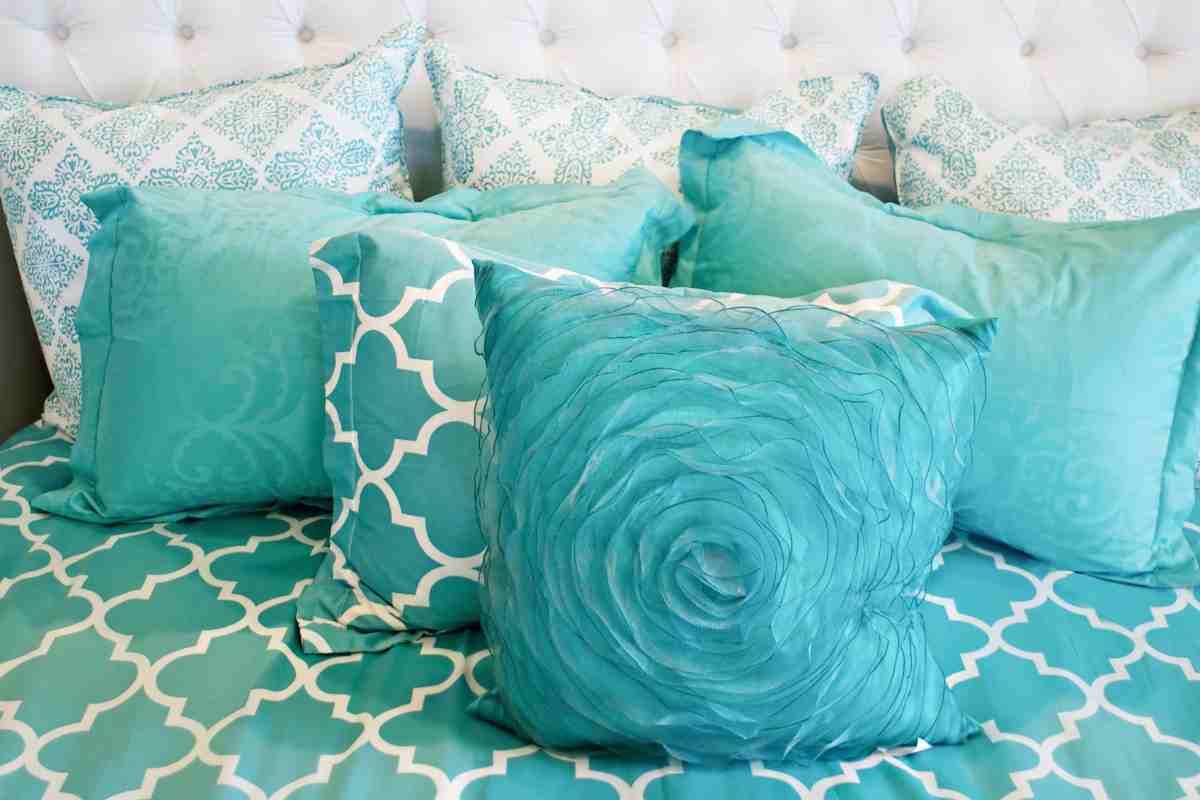 cuscini e coperta sul letto in color ottanio con decorazioni bianche