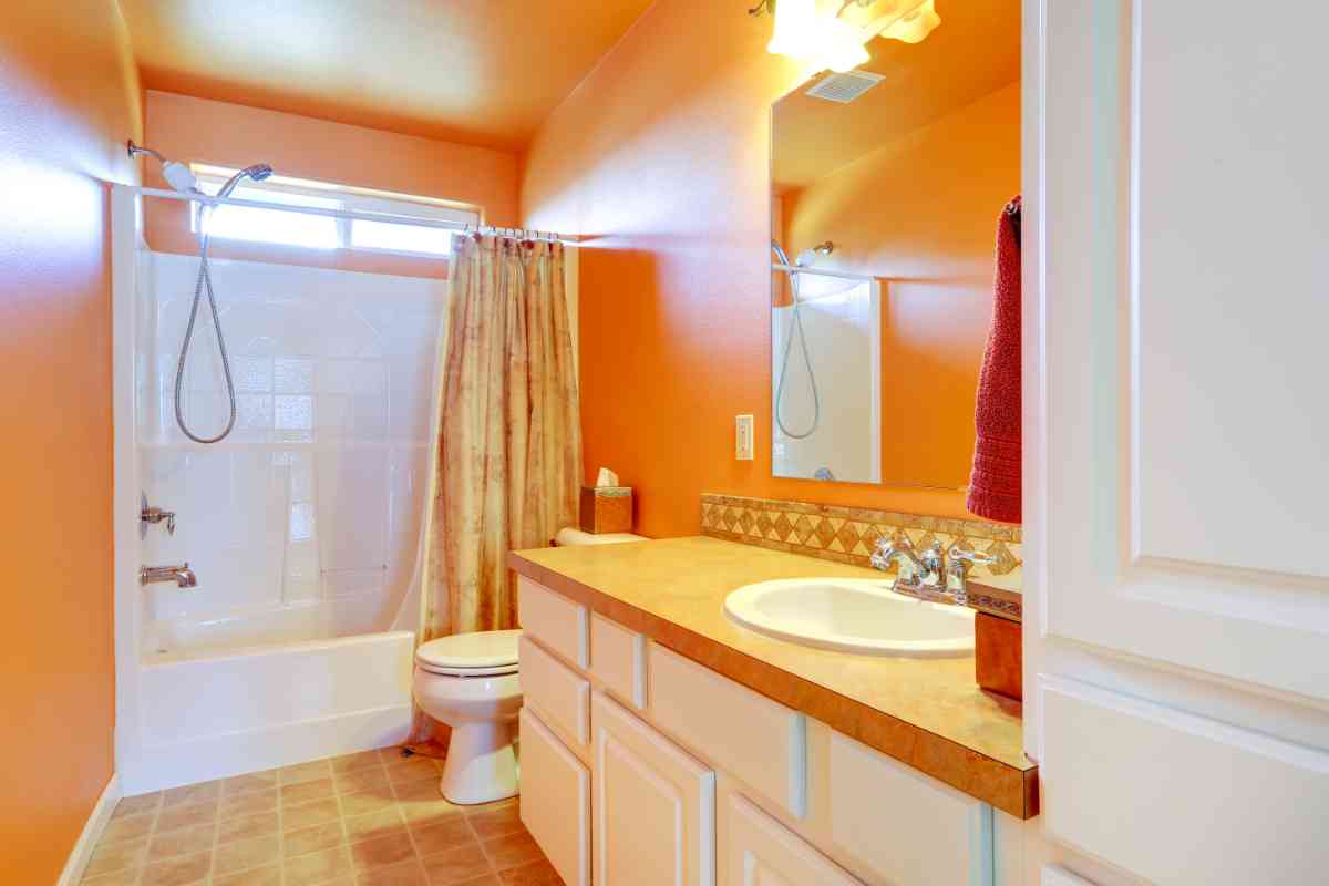 bagno con parete colora arancione e mobili bianchi