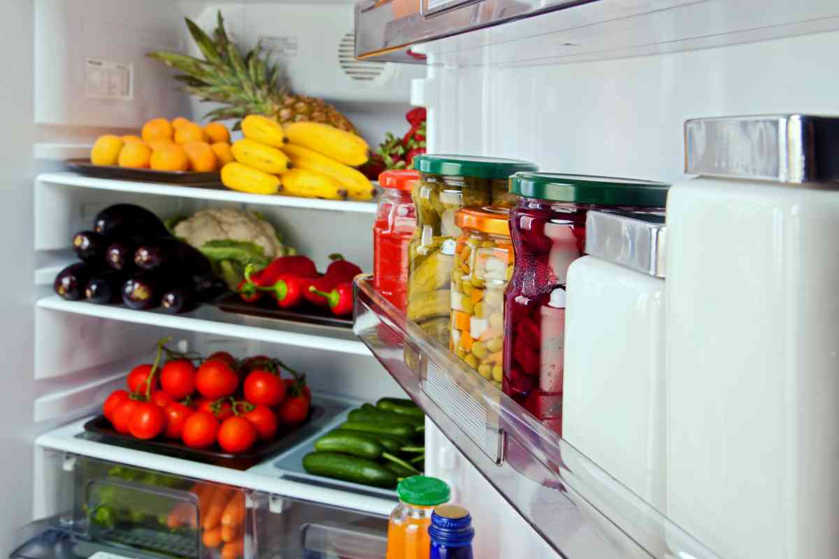 Frigo no frost aperto con verdure e barattoli all'interno