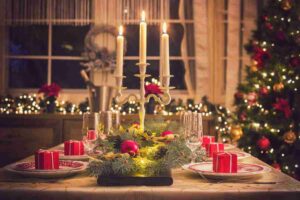 Tavola decorata con colori natalizi come l'oro, oggetti natalizi del catalogo Maisons du Monde di Natale come candele, albero di natale sullo sfondo