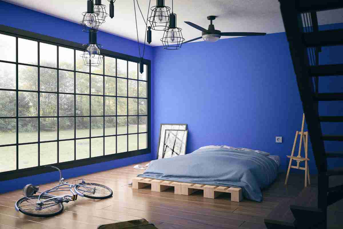 cameretta con parete blu e vetrata, letto su pallet e pavimento in parquet chiaro