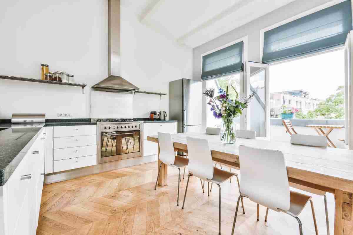 cucina con ampie porte finestre con pareti bianche mobili in legno bianco e parquet