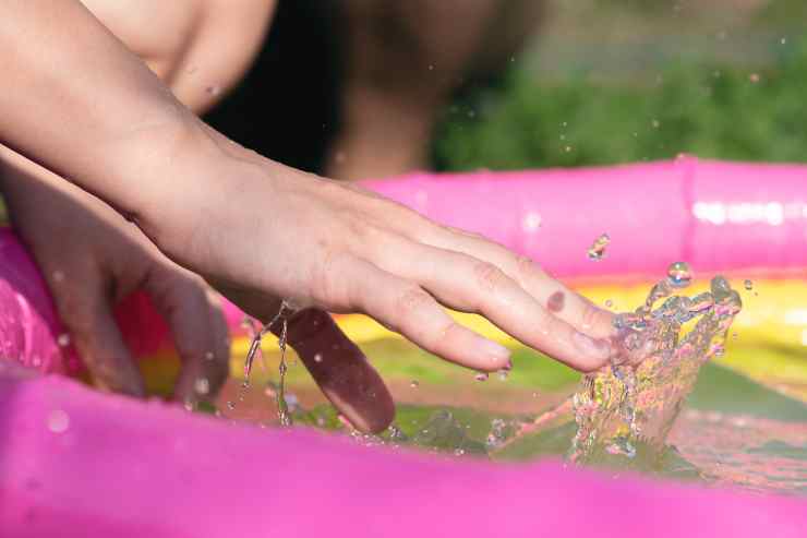 mano bambino che tocca acqua della piscina