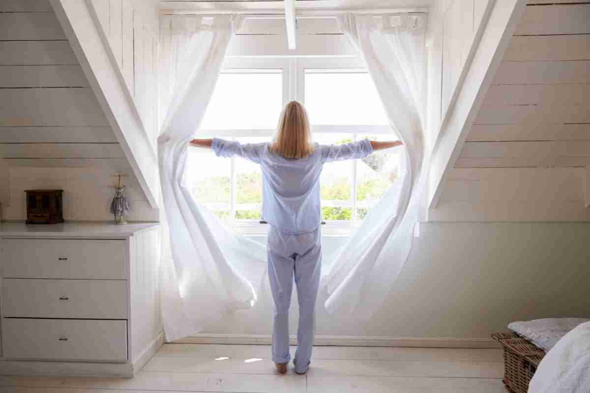 donna sposta le tende e apre le finestre per rimuovere negatività