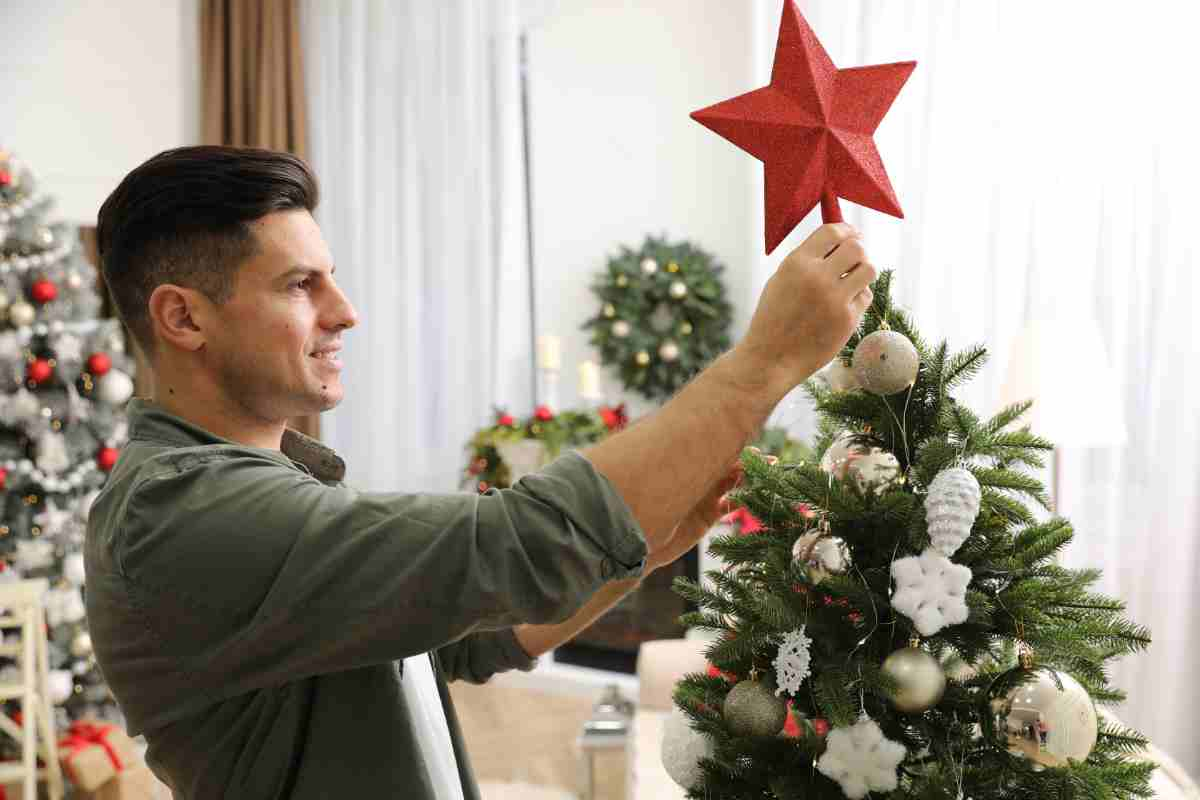 Uomo mette un puntale come simbolo di come scegliere l'altezza giusta dell'albero di Natale 