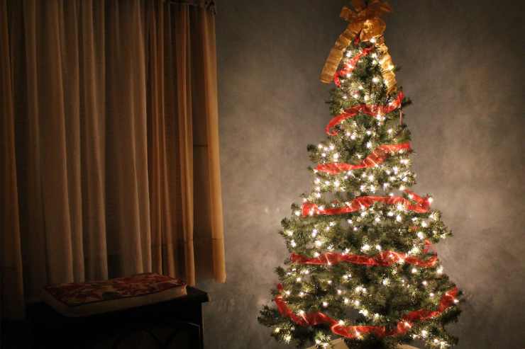 Albero di Natale illuminato decorato con nastro rosso in un angolo della casa