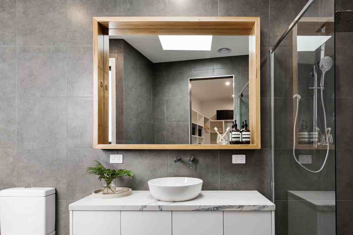 bagno moderno con specchio dalla cornice in legno e illuminazione superiore